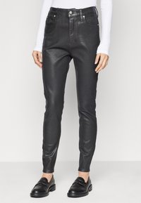 Μαύρο ψεύτικο δερμάτινο κολάν με ψηλή μέση, μπροστινές τσέπες και λεία υφή, διαθέτοντας βρόχους ζώνης και ελάχιστες μεταλλικές λεπτομέρειες.