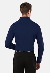 Camicia dress blu navy con una texture liscia, maniche lunghe e colletto classico, abbinata a pantaloni neri con tasche con bottone.