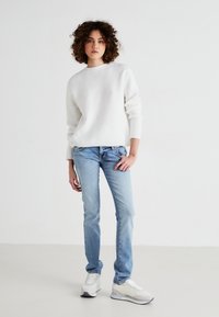 Vit ribbad stickad tröja med långa ärmar, kombinerad med ljusblå slim-fit jeans och vita sneakers med grå detaljer.