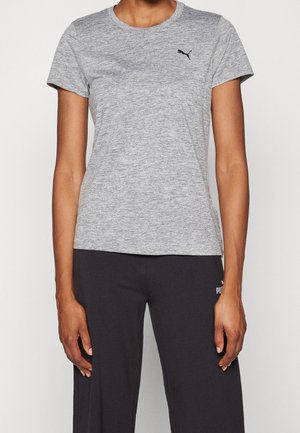 Persoon die een aansluitend grijs Puma T-shirt en losse zwarte Puma broek draagt, staand tegen een effen achtergrond.