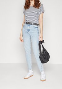 Pruhované tričko s krátkým rukávem, světle modré džíny s vysokým pasem, černý pásek, černá látková taška a bílé tenisky se šedými akcenty.