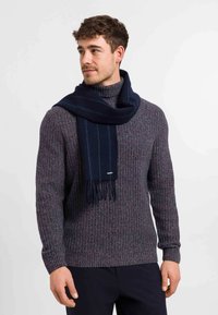 Sciarpa in lana blu navy appoggiata su un maglione in maglia viola mélange. Il maglione presenta una texture a coste e un design aderente, con collo rotondo.