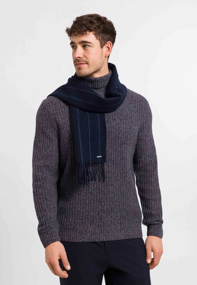 Écharpe en laine marine drapée sur un pull en tricot marbré violet. Le pull présente une texture côtelée et une coupe ajustée, avec un col ras du cou.