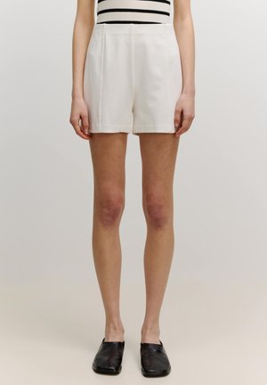 Witte katoenen shorts met een hoge taille, voorzien van plooien en een rechte snit. Gestyld met een zwart-wit gestreepte top en zwarte platte schoenen.