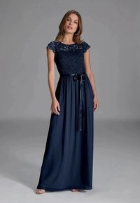 Mujer luciendo un vestido largo de color azul marino con un corsé de encaje, mangas tipo capa y una cinta de satén atada en la cintura.