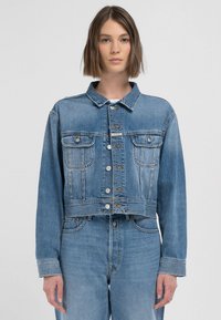 Kort denimjacka i ljusblått med klassisk krage, fyra framfickor och silverfärgad knappstängning, med en vitskatta textur.