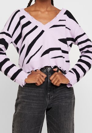 Femme portant un pull court lavande avec des rayures noires irrégulières et des ourlets usés, associé à un jean taille haute gris foncé.