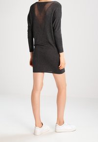 Abito in maglia grigio scuro con maniche lunghe e dettaglio in rete a forma di V sulla schiena, abbinato a sneakers bianche.