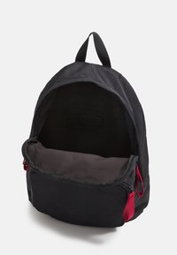 Sac à dos noir avec un extérieur lisse, une poignée supérieure et des accents de fermeture éclair rouges. L'intérieur est non doublé, mettant en valeur un compartiment spacieux.