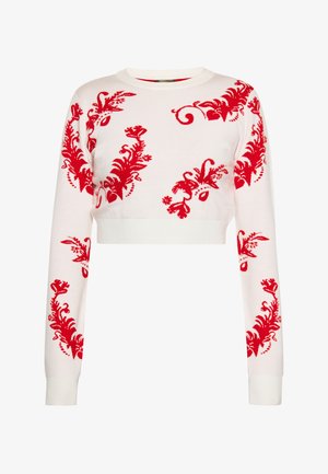 Pull court blanc avec des motifs floraux rouges sur le devant et les manches, avec un col rond et des poignets côtelés.