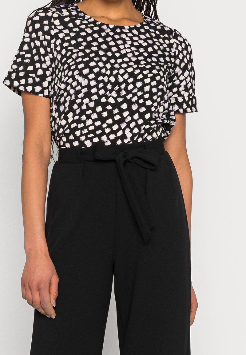 Haut noir avec un motif abstrait blanc et violet, manches courtes, col rond et coupe décontractée, assorti à un pantalon noir taille haute.