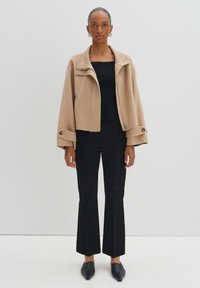 Veste cropped beige avec un col structuré et des accents de boutons, associée à un haut ajusté noir en côtes et un pantalon noir évasé.
