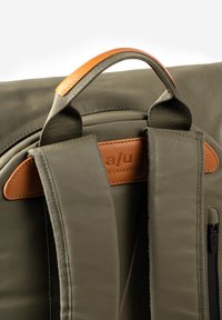 Zaino verde oliva con superficie texture, dotato di manico superiore e spallacci in pelle marrone, e una tasca con cerniera per maggiore funzionalità.