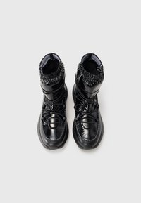 Black waterproof boots with a glossy finish, padded shape, elastic cuff, and functional laces. Textured sole for grip and support.