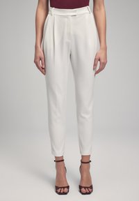 White tailored trousers with a high waist, pleats, and a slim fit. Smooth fabric, cropped length, paired with black strappy heels.