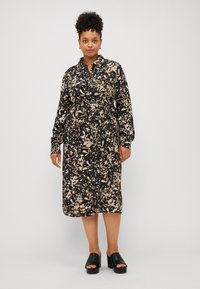 Robe maxi noire avec un imprimé abstrait crème et marron ; dotée d'un devant à boutons, de manches longues et d'une taille cintrée. Portée avec des sandales à plateforme noires.