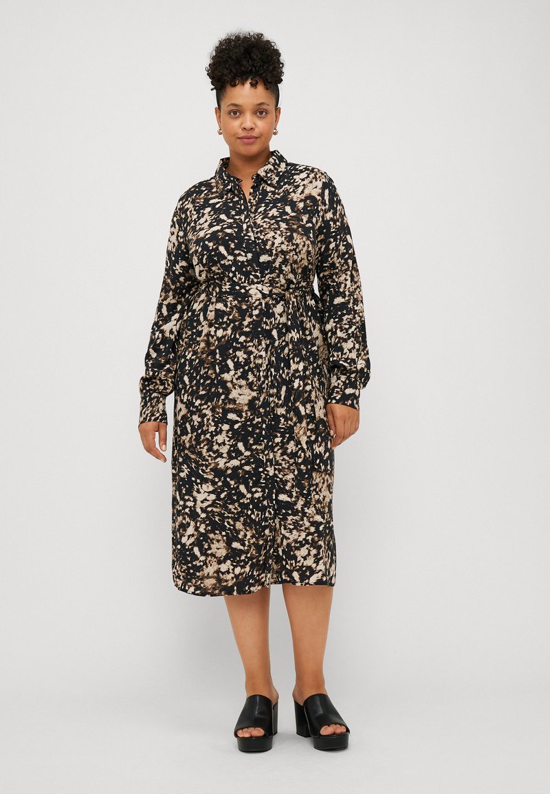Robe maxi noire avec un imprimé abstrait crème et marron ; dotée d'un devant à boutons, de manches longues et d'une taille cintrée. Portée avec des sandales à plateforme noires.