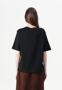 T-shirt nero a maniche corte con una vestibilità comoda e scollatura a girocollo, mostrato da dietro. Il tessuto appare liscio e leggero.