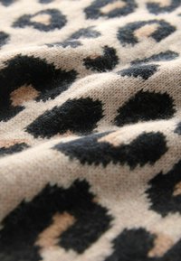 Tissu tricoté beige avec un motif léopard noir et brun clair, montrant la texture et des plis doux.