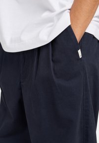 Navy blue cotton shorts with a relaxed fit, featuring side pockets and a small label detail on the waistband. Smooth texture.