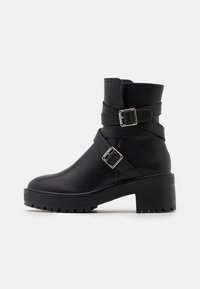 Botas de tobillo de cuero negro con dos correas decorativas y hebillas plateadas. Tacón grueso y suela de goma texturizada para mayor tracción.