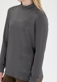 Pitkähihaisessa, korkeakauluksisessa tummanharmaassa paidassa on sileä rakenne. Siinä on hienovarainen täpläkuvio ja kontrastiväriset saumat.