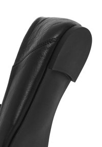 Chaussure en cuir noir avec un bout arrondi et une texture lisse. Elle présente un talon légèrement surélevé avec un dos plat et arrondi.