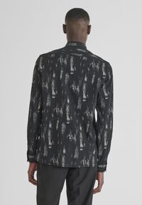 Langarmshirt van zwarte stof met een zilveren abstract patroon; heeft een standaard kraag en geknoopte manchetten, met een aangesloten pasvorm.