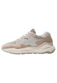 Helle beige Sportschuhe aus einer Mischung aus Wildleder und Mesh, mit einem markanten Logo, strukturierten Akzenten und einer dicken Plattformsohle.