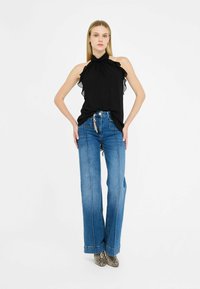 Top nero con scollatura a halter e dettagli a rouches, abbinato a jeans blu a vita alta e a gamba larga, e stivaletti alla caviglia in pelle di serpente con texture.