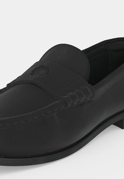Μαύρο δερμάτινο slip-on loafer με ραμμένες λεπτομέρειες και διακριτικό ανάγλυφο έμβλημα στο πάνω μπροστινό μέρος.