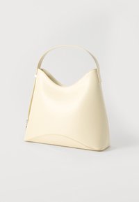 Κρεμ δερμάτινη τσάντα ώμου με καμπύλη πάνω άκρη και έναν φαρδύ ιμάντα, που εμφανίζεται σε απλό ανοιχτό φόντο.