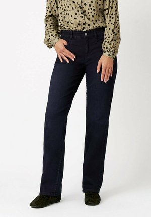 Marineblaue Denim-Jeans im geraden Schnitt mit klassischer Passform, kombiniert mit einer leichten, cremefarbenen Bluse mit schwarzen Pünktchen.