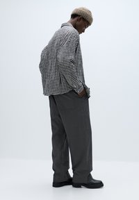 Ternede langærmede skjorte i sort og hvid med løs pasform, kombineret med grå bukser med vid ben og sorte støvler. Ulden beige beanie bæres.