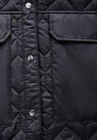 Schwarze gesteppte Jacke mit einem Rautenmuster, ausgestattet mit silbernen Druckknöpfen und zwei Fronttaschen. Glatte Textur, leichtes Material.