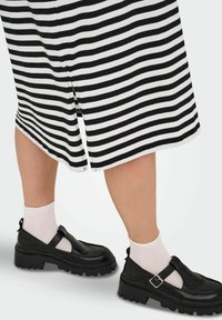 Černobílé pruhované šaty s bočním rozparkem, doplněné o černé robustní boty a bílé kotníkové ponožky. Důraz na strukturu a designové prvky.