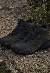 Czarne buty wędkarskie wykonane z materiałów syntetycznych, z teksturowaną powierzchnią, wzmocnionym czubkiem oraz grubą podeszwą z wytrzymałym wzorem.