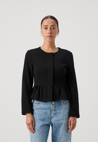 Juoda peplum striukė su ilgomis rankovėmis, apvaliu iškirpimu ir priekyje užsegama mygtuku, derinama su šviesiai mėlynomis džinsinėmis kelnėmis. Paprastas, elegantiškas dizainas.