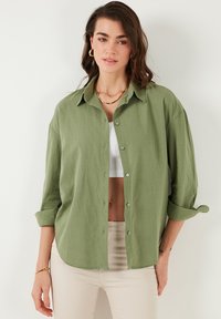 Light green, button-up shirt with a relaxed fit, featuring a collared neckline and rolled-up sleeves. Made of soft, textured fabric.