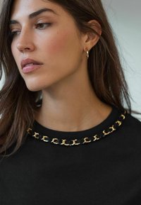 Top noir avec un col rond orné d'un motif de chaînes dorées. Le tissu semble lisse et le design est simple et élégant.