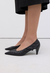 Black leather kitten-heeled pumps with a pointed toe and gathered edge detail, showcasing a smooth texture and streamlined design.