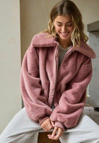 Faux fur jakke i blød lyserød med en stor krave, lynlås foran og ribbede manchetter. Har en luksuriøs tekstur og oversized pasform.