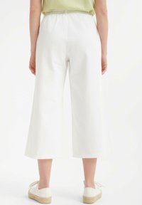 Pantalones blancos de pierna ancha, hechos de una tela ligera, con una cintura elástica. Zapatos en un tono neutro con una suela texturizada.