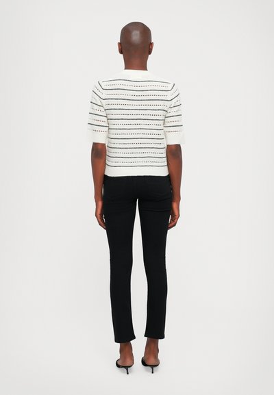 Witte gebreide trui met zwarte strepen, korte mouwen en een aansluitend design; gecombineerd met zwarte rechte broek en hoge hakken.