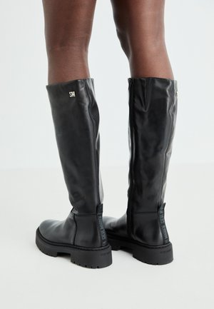 Schwarze knielange Lederstiefel mit glatter Textur, abgerundetem Zeh, robustem Absatz und Reißverschluss. Mit silbernem Logo an der Seite.