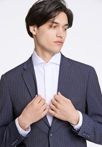 Marinblått pinstripe kostymjacka tillverkad av tyg med en slät textur, i kombination med en vit skjorta med knappar och kontrasterande manschetter.