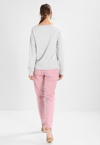 Maglione grigio chiaro con vestibilità morbida, abbinato a pantaloni rosa chiaro e tacchi beige. Texture del tessuto liscia; design minimalista.