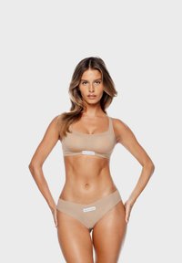 Bralette beige sans couture et culottes taille haute avec logo. Matériau doux, design ajusté, texture lisse. Pas de coutures ou motifs visibles.
