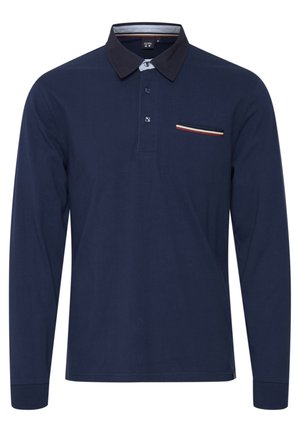 Tummansininen pitkähihaisena polo-paita, joka on valmistettu puuvillasta. Paidassa on erivärinen kaulus, kolme nappia ja rintatasku värillisin raidoin.