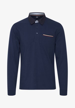 Tummansininen pitkähihaisena polo-paita, joka on valmistettu puuvillasta. Paidassa on erivärinen kaulus, kolme nappia ja rintatasku värillisin raidoin.